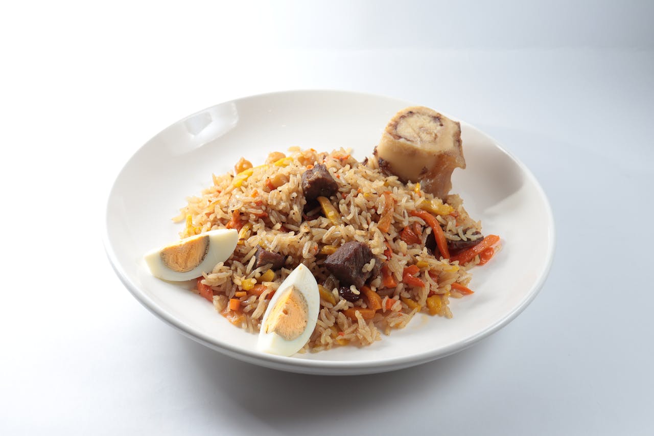 A savory dish of jollof rice served with meat, vegetables, and boiled eggs on a white plate.